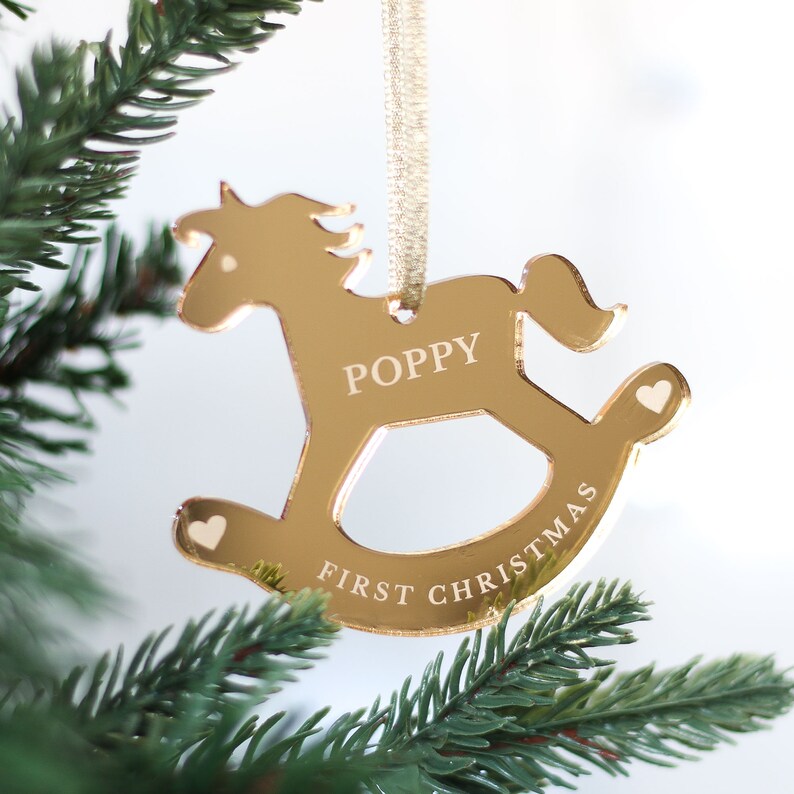 Puede incluir: Adorno de Navidad de caballo de balanc&iacute;n de espejo dorado con el nombre "Poppy" y el texto "First Christmas" en la base.