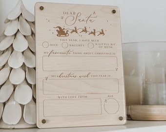 May include: A wooden sign with a Santa Claus design and the text "Dear Santa". The sign has a section for a child to write their Christmas wish and a section for them to write their favorite thing about Christmas. There are also sections for the child to write their age and for a parent to write "With love from".