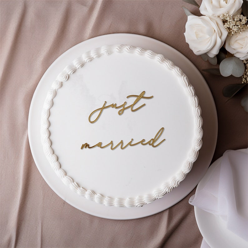 May include: A white wedding cake with gold lettering that says "just married" on top.