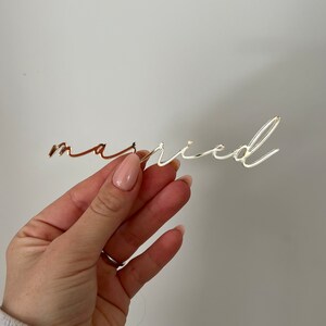 May include: Gold-colored metal word "married" in a cursive font.