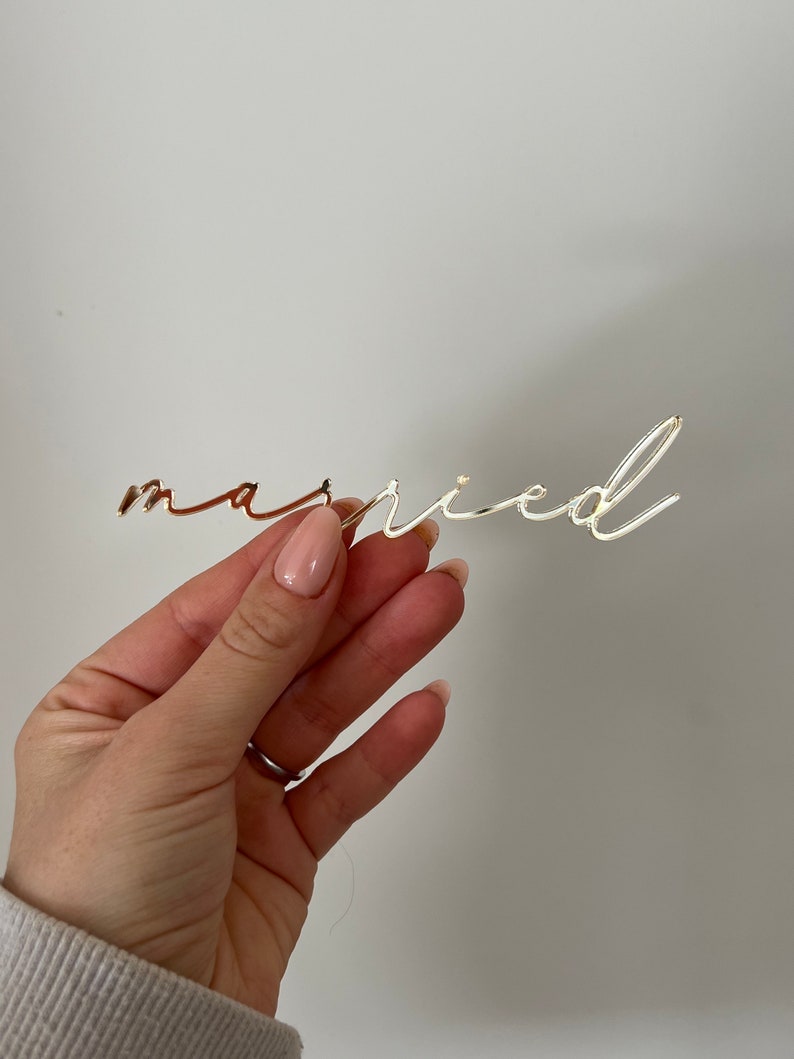 May include: Gold-colored metal word "married" in a cursive font.