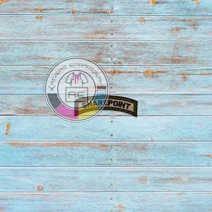 May include: A blue wooden background with a white and pink circle logo that says "River's Embroidery" and a brown patch that says "Sharpoint".