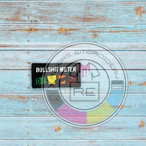 Könnte beinhalten: Ein schwarz-weißes Patch mit dem Text "Bullshit Meter" und einer Reihe von farbigen Symbolen. Das Patch befindet sich auf einem blauen Holzgrund mit einem kreisförmigen Logo, auf dem "Embroidery Lovers" steht.