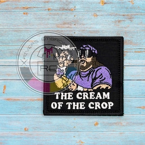 May include: Black embroidered patch with a cartoon image of a man with a beard and sunglasses wearing a purple shirt. The text "The Cream of the Crop" is below the image.