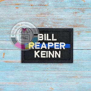 May include: Black embroidered patch with white text that reads "Bill Reaper Kein" with a thin blue line above the text.