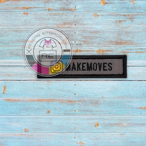 May include: A black and gray embroidered patch with the text "MAKEMOVES" on a light blue wood background.