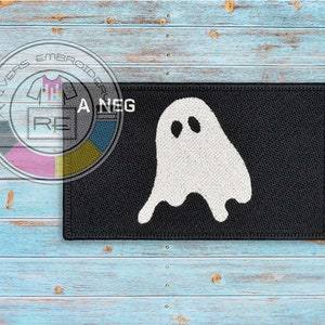 Puede incluir: Un parche bordado negro con un diseño de fantasma blanco. El parche tiene un contorno blanco y el fantasma tiene dos pequeños ojos negros.