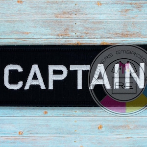 May include: Black embroidered patch with white text that reads "CAPTAIN".