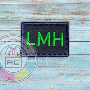 May include: A black and navy blue embroidered patch with the letters LMH in green.