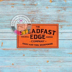 Può includere: Un cartello arancione con testo nero che recita "The Steadfast Edge Company. Stilwell, Kansas. Knife and Tool Sharpening."
