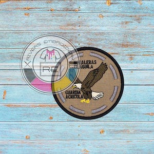 May include: A brown and gray embroidered patch with a bald eagle with its wings spread. The eagle is flying over the text "Guardia Agricola" and "Taleras Aguila".