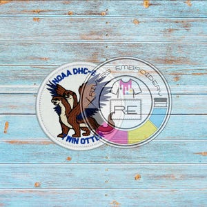 May include: Two embroidered patches on a blue wooden background. One patch features a brown and blue otter with the text "NOAA DHC" and "WIN OTTER". The other patch has the text "RIVERS EMBROIDERY" and "RE" in a circle.