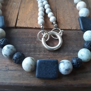 May include: A necklace made with white, gray, and black beads. The necklace has a silver clasp and is made with natural stones.