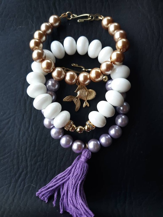 Set of 3 beaded stackable bracelets with glass pearls in gold, purple and white, a purple tassel, gold tone fish charm
