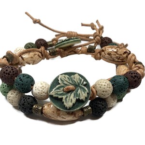 May include: A brown leather bracelet with green, white, and brown beads. The bracelet has a green ceramic button with a leaf design.