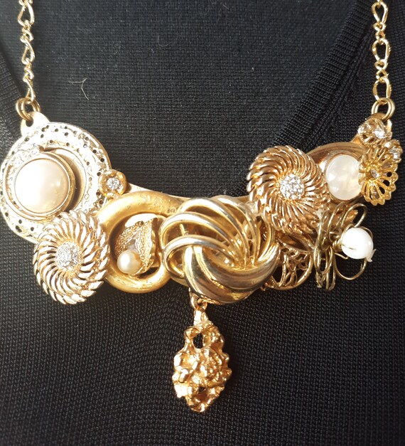 Assemblage necklace using vintage earrings, cuff links and brooches in gold tone and white with gold tone chain and toggle closure