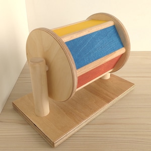 May include: A wooden toy with a spinning wheel and colorful stripes. The wheel is painted yellow, blue, and red. The toy is mounted on a wooden base.