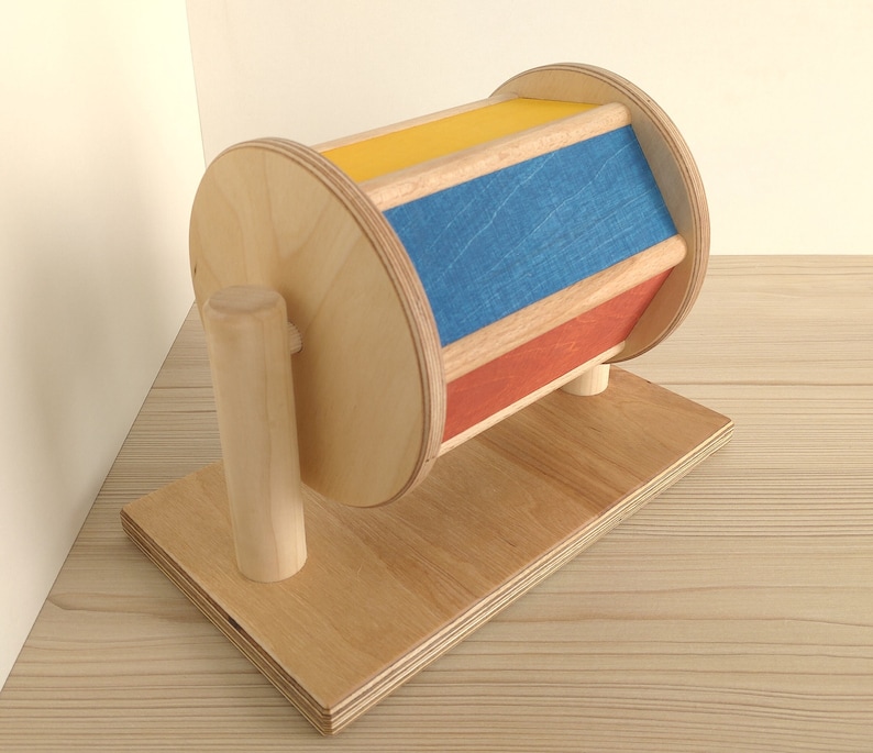 May include: A wooden toy with a spinning wheel and colorful stripes. The wheel is painted yellow, blue, and red. The toy is mounted on a wooden base.
