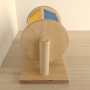 May include: A wooden toy with a spinning wheel. The wheel is painted yellow and blue. The toy is on a wooden base with a wooden handle.