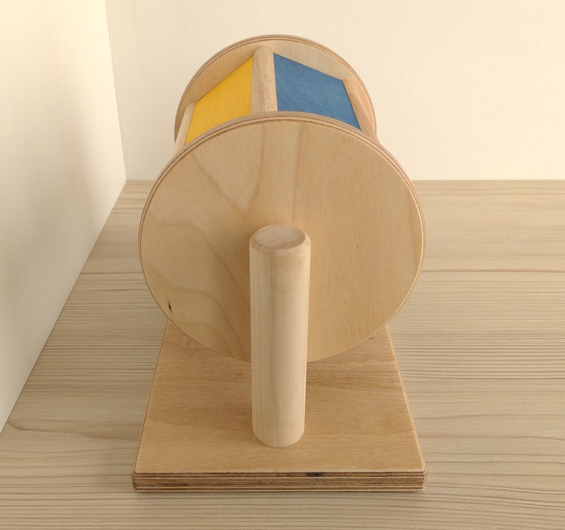May include: A wooden toy with a spinning wheel. The wheel is painted yellow and blue. The toy is on a wooden base with a wooden handle.