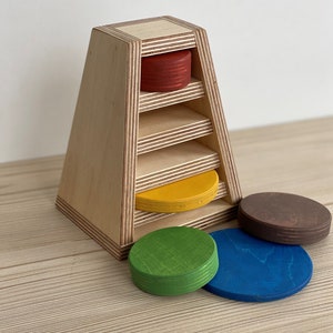 May include: Wooden stacking toy with five colorful circles. The circles are red, yellow, green, blue, and brown. The toy is made of wood and has a triangular base.