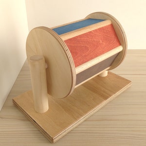 May include: A wooden toy with a spinning wheel. The wheel is painted in red, blue, and brown stripes. The toy is mounted on a wooden base.