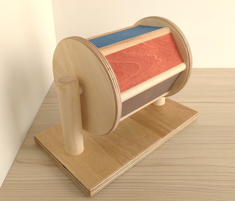 May include: A wooden toy with a spinning wheel. The wheel is painted in red, blue, and brown stripes. The toy is mounted on a wooden base.