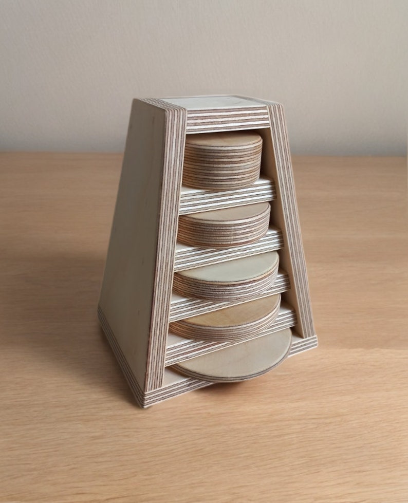 May include: A wooden tower with six circular shelves, each made of layered plywood. The tower is a light wood color and has a triangular shape.