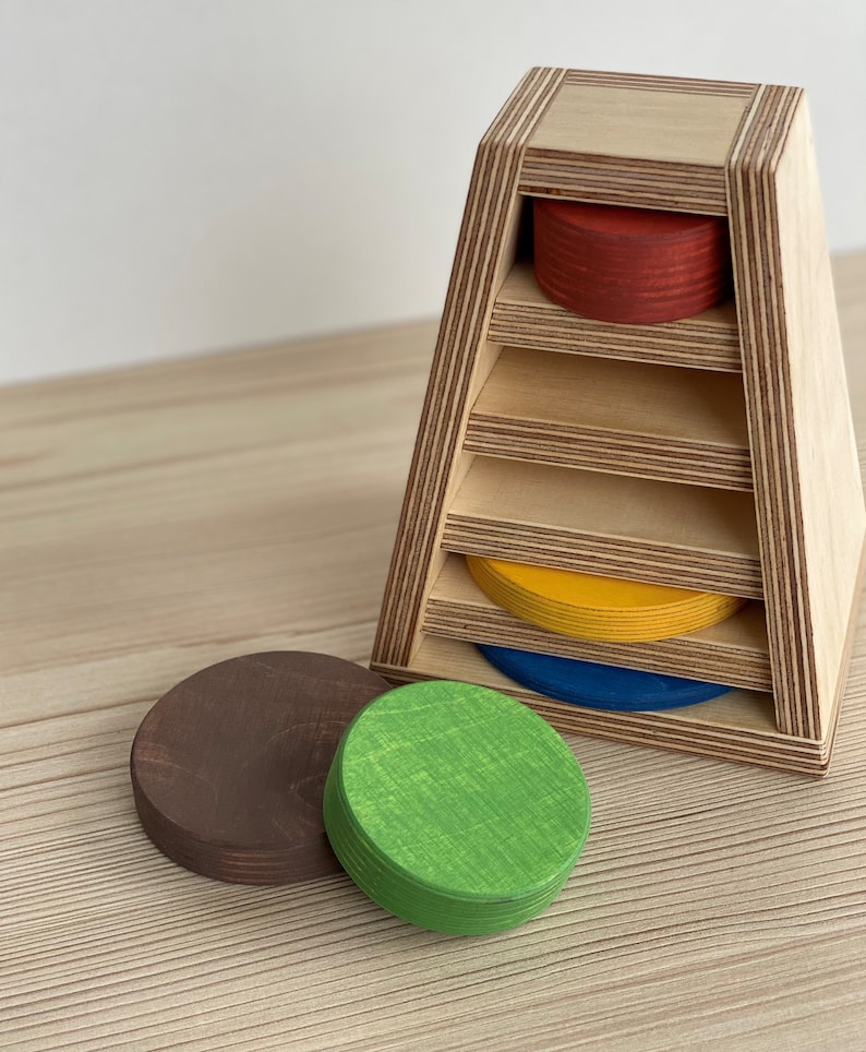 May include: Wooden toy with five colorful circular pieces that fit into a triangular wooden frame. The pieces are red, yellow, blue, green, and brown.
