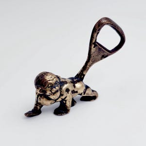 Puede incluir: Un abridor de botellas de mono de latón con una figura de mono detallada y un abridor de botellas funcional.