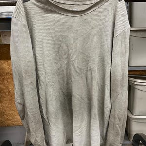 May include: A gray long-sleeved waffle knit shirt hanging on a metal rack.
