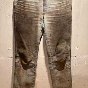 May include: A pair of blue denim jeans with brown stains and dirt marks. The jeans are worn and have a faded appearance.