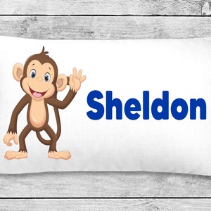 May include: White pillow with a brown monkey cartoon waving and the name Sheldon in blue letters.