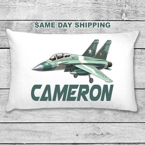 May include: White pillow featuring a green camouflage fighter jet and the name "CAMERON" in green text.