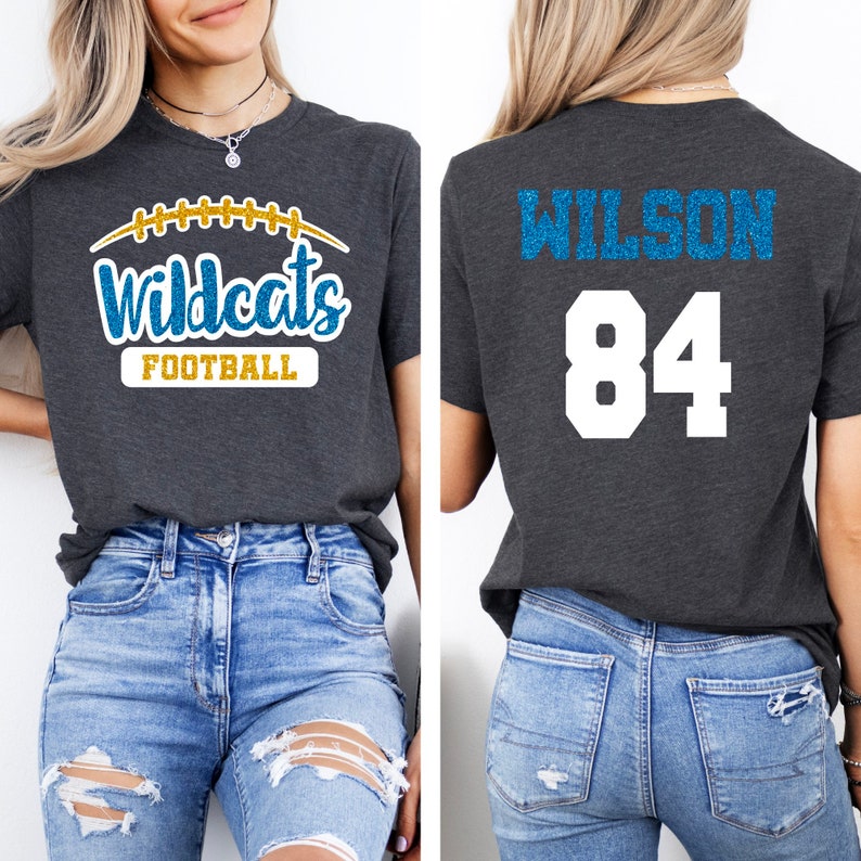May include: A dark gray t-shirt with a blue and gold glitter design that says "Wildcats Football" on the front and "Wilson 84" on the back.