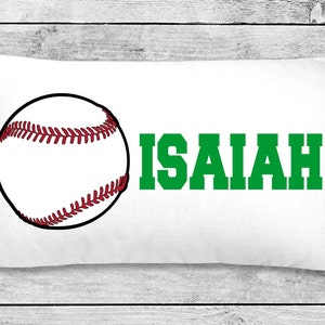 May include: White rectangular pillow featuring a baseball graphic and the name "ISAIAH" in green block letters. The baseball is white with red stitching and a black outline. The pillow is on a white wooden surface.