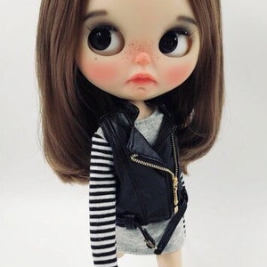 May include: A doll with brown hair wearing a black leather jacket, a striped shirt, black socks, and black sneakers.