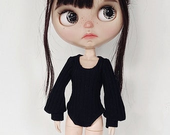 May include: A black doll with long black hair styled in two buns. The doll is wearing a black long-sleeved bodysuit and black shoes.