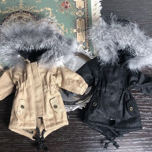 May include: Two miniature hooded winter coats with faux fur trim. One coat is beige and the other is black.