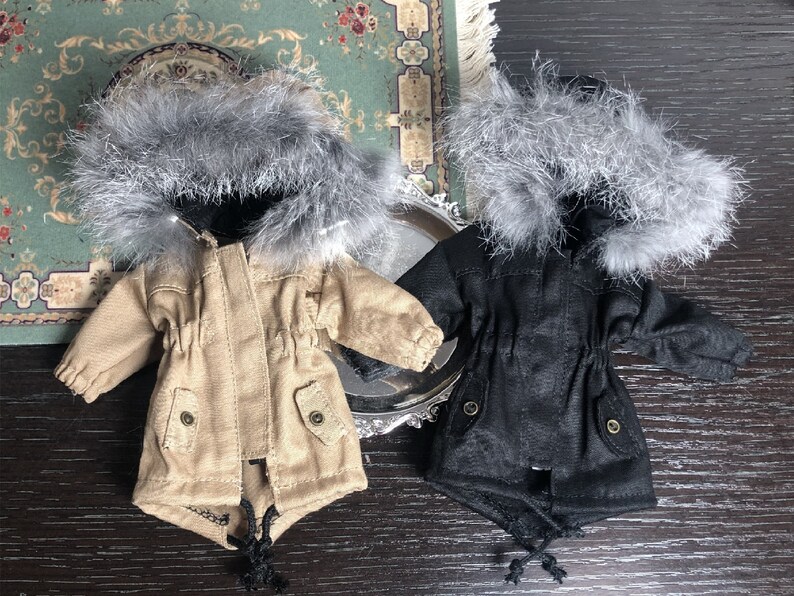 May include: Two miniature hooded winter coats with faux fur trim. One coat is beige and the other is black.