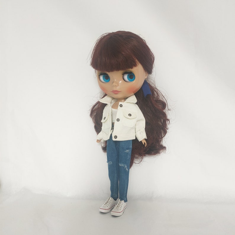 May include: A doll with long brown hair wearing a white denim jacket, blue jeans, and white sneakers.