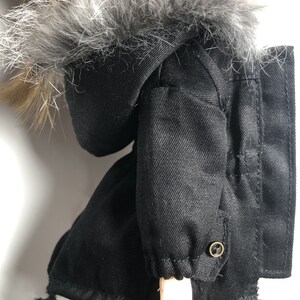 May include: Black hooded jacket with a faux fur trim around the hood. The jacket has a drawstring at the bottom and a button on the sleeve.