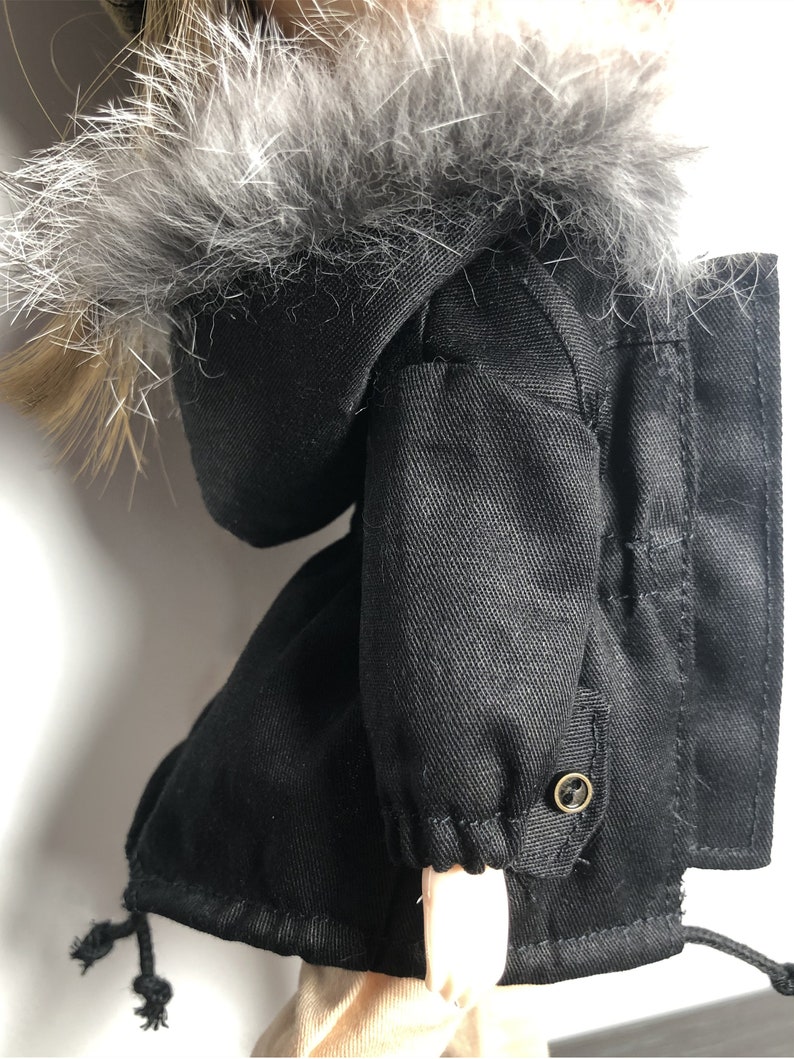 May include: Black hooded jacket with a faux fur trim around the hood. The jacket has a drawstring at the bottom and a button on the sleeve.