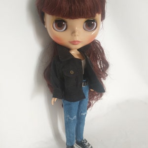 May include: A doll with long brown hair wearing a black corduroy jacket, blue jeans, and black shoes.