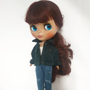 May include: A doll with long, dark brown hair wearing a dark green corduroy jacket and blue jeans. The doll has blue eyes and a light pink blush.