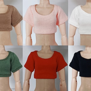 Op de afbeelding: Zes gecropte T-shirts in verschillende kleuren: bruin, roze, wit, groen, rood en zwart. De shirts hebben korte mouwen en een ronde hals.