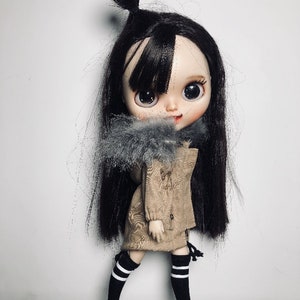 May include: A doll with long black hair, wearing a brown jacket with a grey fur collar, black and white striped socks, and black trainers.