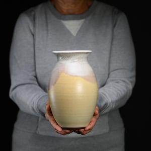 May include: A ceramic vase with a rounded body and a flared rim. The lower portion of the vase is a solid matte yellow, while the upper section features a smooth, speckled white glaze that drips down over the yellow surface in a soft gradient.