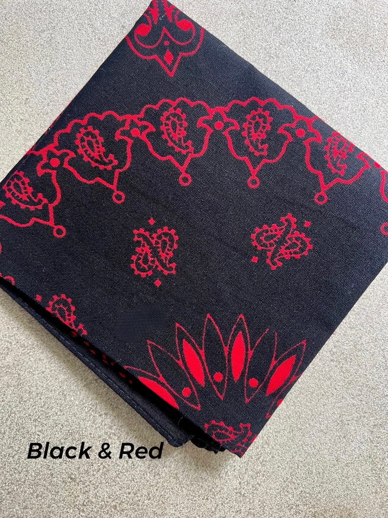 May include: Black and red bandana with a paisley pattern. The bandana is folded and features a repeating design of red paisley shapes on a black background. The text "Black & Red" is visible.