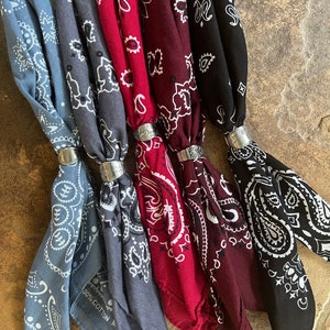 May include: A collection of six bandanas in various colors, including light blue, gray, burgundy, and black. Each bandana features a white paisley pattern and is held together with a silver-colored ring. The bandanas are made of 100% cotton.